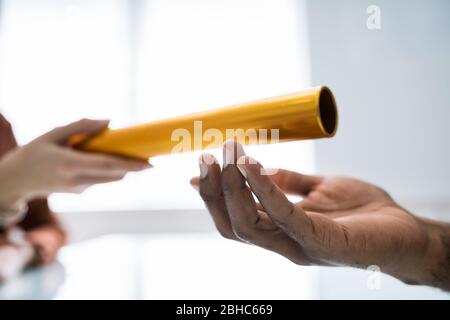 Close-up Of Businessman's Hand Passing The Golden Baton To His Partner In Office Stock Photo