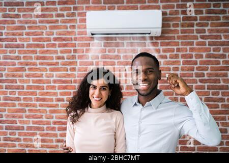 Portrait Of Happy Couple Holding Remote Control Air Conditioner Stock Photo