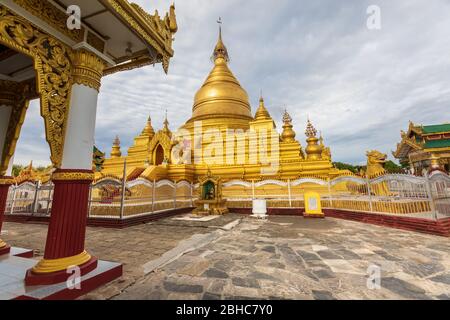 Mandalay, Myanmar. July 24, 2019: Kuthodaw Pagoda, golden yellow Buddhist religious structure in the Mandalay region of Burma. Cloudy sky. Stock Photo