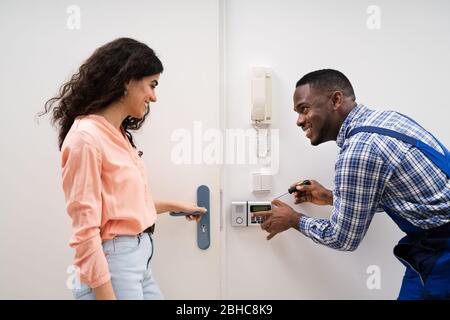Close-up Of Handyman Installing Security System Near Door Wall While Woman Using Remote Stock Photo