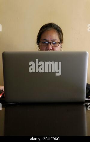 Photo of a Filipino woman working on a laptop computer at home. Stock Photo