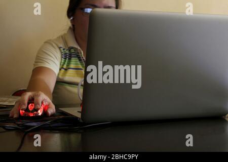 Photo of a Filipino woman's hand holding a computer mouse while working on a laptop computer at home. Stock Photo