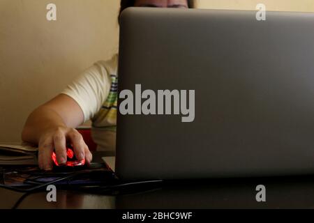 Photo of a Filipino woman's hand holding a computer mouse while working on a laptop computer at home. Stock Photo