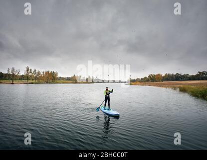 Man training on paddleboard in the lake against overcast sky Stock Photo