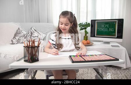 The girl is sitting at the table and doing homework. The child learns at home. Home schooling. Stock Photo