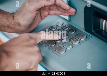 Man entering a PIN code for his credit card at an ATM, withdrawing money, finance concept Stock Photo