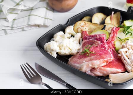 Natural organic fresh raw ingredients meat, vegetables and mushroom on a black ceramic plate for cooking dinner on a white wooden background, served f Stock Photo