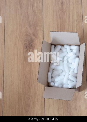 A cardboard box with packing foam pellets top view, on wooden floor Stock Photo