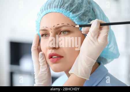 Plastic surgeon applying marks on woman's face in clinic Stock Photo