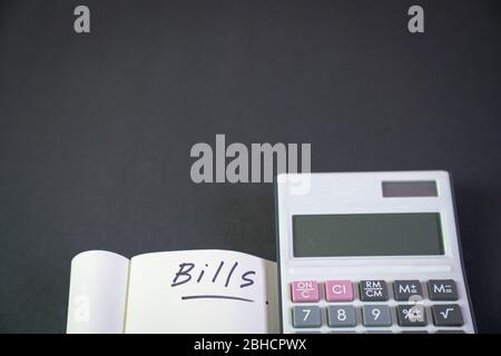Notepad with the words, Bills with calculator by the side. Black background. top view. Stock Photo