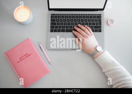 Top view of pink notebook and laptop on white desk with hand typing on keyboard. Stock Photo