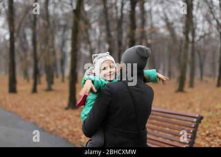 Mother carrying a toddler daughter in the autumn park