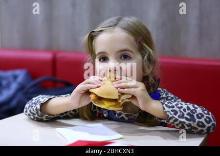 Portrait of a caucasian four year old girl eating burger in a cafe Stock Photo