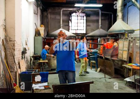 Venice, italy - 20 january 2020: italian artisan glassworker blowing hot glass with traditional, blowpipe in an italian glass factory, symbol of itali Stock Photo