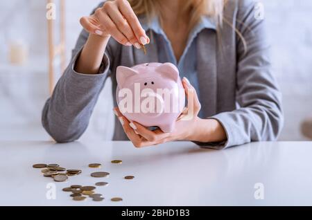 Savings for crisis. Woman puts money in piggy bank. Stock Photo