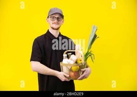 Handsome courier in black uniform and cap holds basket with fresh farm products Stock Photo