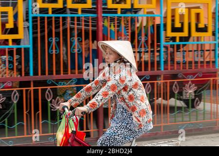 Middle aged Vietnamese woman wearing traditional conical hat , non la , riding a bicycle , Sa Dec,  Mekong Delta , Vietnam, Asia Stock Photo