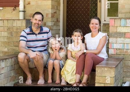 A smiling Zimbabwean family living in Australia sit at the front steps of their Sydney home during the Covid-19 epidemic. Stock Photo