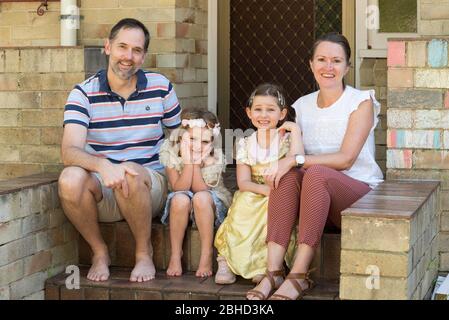 A smiling Zimbabwean family living in Australia sit at the front steps of their Sydney home during the Covid-19 epidemic. Stock Photo