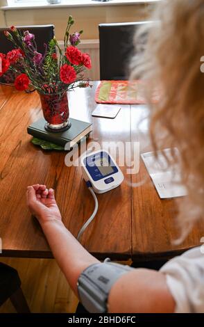 Middle aged woman using an Omron Blood Pressure testing monitor at home  Photograph taken by Simon Dack Stock Photo