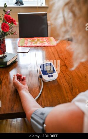 Middle aged woman using an Omron Blood Pressure testing monitor at home  Photograph taken by Simon Dack Stock Photo