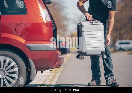 Man getting ready for holiday, vacation, putting a luggage into the car trunk, leisure time, tourism concept Stock Photo