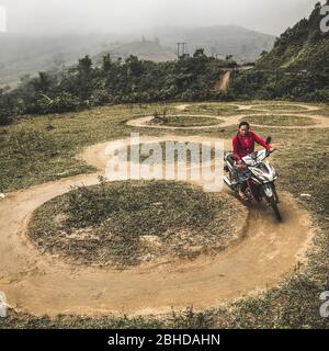 Pa Cheo, Hoang Lien Son, Vietnam, January 4, 2020 - Young woman learning to ride a motorcycle without a helmet on a grass field by making circles Stock Photo