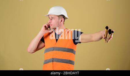 Man supervises construction on phone, ocher background. Supply of building materials concept. Engineer, architect on busy face speaks on phone, holds blueprints, pointing with finger, copy space Stock Photo