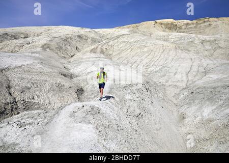 Runner athlete with beard running on the trail at white clay mountains in the desert