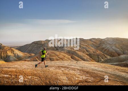 Runner athlete with backpack running on the wild trail at red mountains in the desert Stock Photo