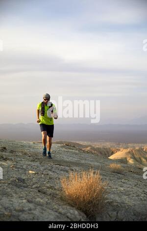 Runner athlete with backpack running on the wild trail at red mountains in the desert Stock Photo