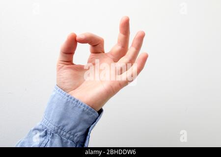 Man's hand in a blue shirt touching or pointing to something on white wall background. Close up. Copy space Stock Photo