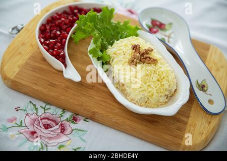 Traditional Russian salad Mimoza. Isolated on wooden background. Top view. CHICKEN SALAD with walnuts and mushrooms . Granulated pomegranate Stock Photo