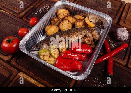 Appetizing mackerel fish baked on fire with spices, served on a plate and decorated with vegetables on wooden background Stock Photo