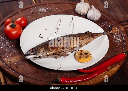 Appetizing mackerel fish baked on fire with spices, served on a plate and decorated with vegetables on wooden background Stock Photo