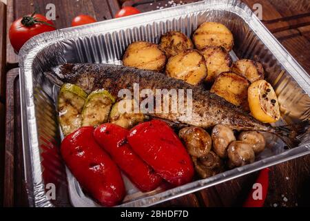 Appetizing mackerel fish baked on fire with spices, served on a plate and decorated with vegetables on wooden background Stock Photo
