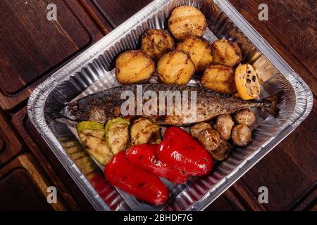 Appetizing mackerel fish baked on fire with spices, served on a plate and decorated with vegetables on wooden background Stock Photo
