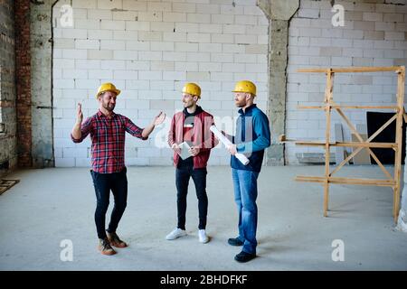 Happy young engineer or builder explaining his colleagues what else can be done about furnishing of walls at working meeting Stock Photo