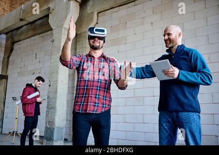 Young engineer in vr headset making presentation of new system of building and furnishing materials to his colleague at meeting Stock Photo