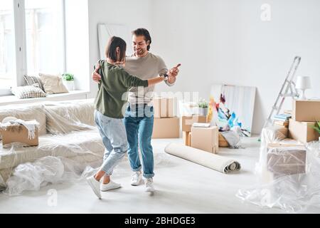 Young affectionate couple in casualwear dancing in living-room after removing to new flat or house with packed stuff on background Stock Photo