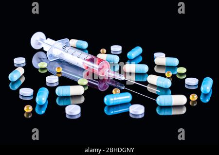 5 ml plastic medical syringe with a stainless steel needle filled with red liquid (blood) and different multi-colored tablets, pills and capsules on a Stock Photo