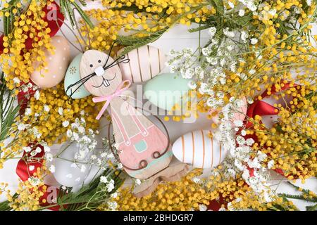 Creative Easter layout made of eggs and flowers on white wooden background. Yellow mimosa and small little flowers flat lay concept Stock Photo