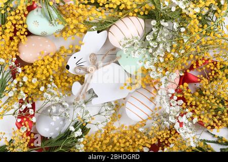 Creative Easter layout made of eggs and flowers on white wooden background. Yellow mimosa and small little flowers flat lay concept Stock Photo