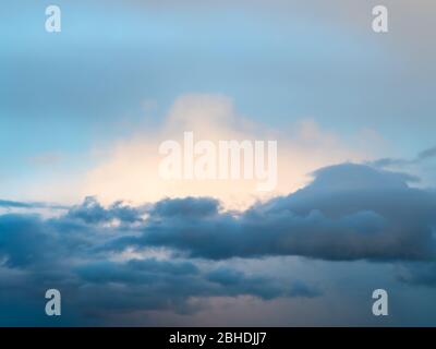 dark clouds in front of white sunlit cloud in blue sky at spring dusk Stock Photo