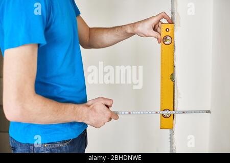 Man using a spirit level to plumb a wall. Home renovation concept. checks wall level. Man with tape measure in new flat with concrete walls Stock Photo
