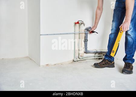 Plumbing in the house. Installation of sewer pipes in the kitchen of an apartment interior during renovation works. Man with tape measure in new flat Stock Photo