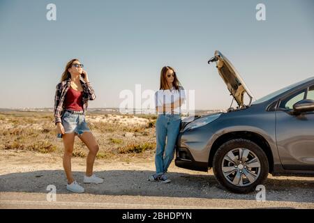 Female friends examining broken down car on country road Stock Photo