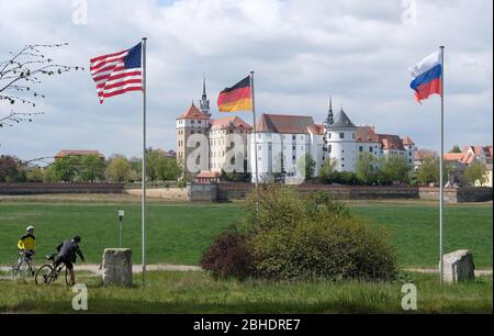 Torgau, Germany. 25th Apr, 2020. The US, German and Russian flags are waving on the banks of the Elbe, with Hartenfels Castle in the background. On the occasion of the 75th anniversary of the meeting of American and Soviet soldiers on April 25, 1945 - the so-called Elbe Day - a commemorative event took place in Torgau, which, due to the corona pandemic, took place in a small circle and was broadcast online. Credit: Sebastian Willnow/dpa-Zentralbild/dpa/Alamy Live News Stock Photo