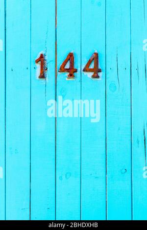 House number 144 on a bright blue wooden gate Stock Photo