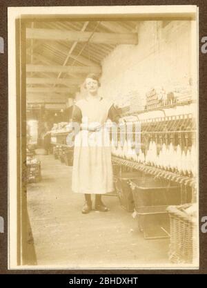 Early 1900's photograph of Lancashire cotton spinner, standing next to a spinning mule  in a cotton mill, wearing clogs, Radcliffe, Lancashire, U.K. circa 1917